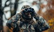 A man in full camouflage stands looking through binoculars while bowhunting
