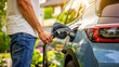 © thanakrit - Man in casual attire charging electric vehicle with power cable in a residential driveway