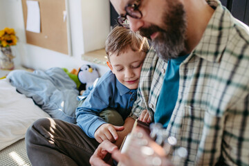 Father teaching boy to play on acoustic guitar. Mesmerized son listening dad making music. Concept of Fathers Day and fatherly love.