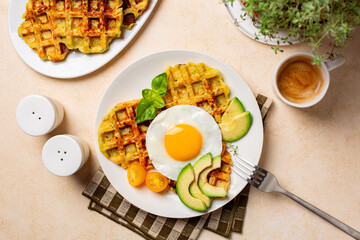 Wall Mural - Homemade breakfast or brunch. Fried egg with belgian waffles made with cheese and vegetables, zucchini, onion, carrot, served with avocado and yellow tomato. Cup of coffee drink.