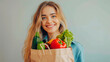 Portrait of a young woman - a happy blonde with long wavy hair and a snow-white smile holding a paper bag of vegetables and groceries on a light background.