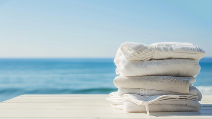 Wall Mural - Stack of folded towels on table with copy-space for text. A lot of stacked towels in white color tones were displayed on a beach background.