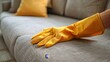 © iuricazac - Hand wearing yellow glove resting on gray upholstered couch.