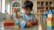 Young child engrossed in play with colorful wooden building blocks creating a tower on a wooden table in a brightly lit room with shelves filled with toys and books in the background.
