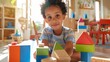 © iuricazac - Young child with curly hair wearing a striped shirt sitting on the floor with colorful wooden blocks surrounded by toys in a brightly lit room.