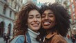 Two smiling women with curly hair one with brown and the other with black embracing each other on a city street with blurred background.