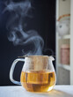 steaming glass jug with infusion or hot tea in a golden filter
