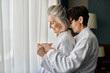 Senior lesbian couple share a quiet moment by the window.