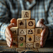 © AmayaGB - Persona sujetando con sus manos unos tacos de madera con diferentes símbolos refiriendo varias industrias, energética, reciclaje, economía, producción, construcción, medios, recursos, materias primas