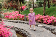 Little girl in stylish dress walking in summer garden with pink flowers.