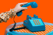 © VISTA by Westend61 - Hand of woman picking up telephone receiver against orange background