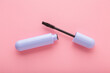 Opened purple tube of black eyes mascara on light pink table background. Pastel color. Female beauty product. Closeup. Top down view.