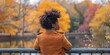 © Svitlana - Back view of thoughtful African American female in coat leaning on fence near pond enjoying view while standing in city park on autumn day