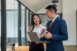 © Wasana - Focused businesswoman holding a laptop while discussing with a colleague, highlighting teamwork and digital workflow in a modern office.