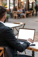 Wall Mural - Profile view of a businessman utilizing a laptop with a blank white screen while seated in a café, illustrating the concept of remote work and modern lifestyles