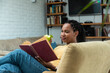 Simple living. African American woman reading book and eating apple in living room. Healthy life and enjoyment at home in free time. Book lover quality time