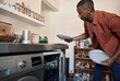 Young African man putting plates in a dishwasher in his kitchen