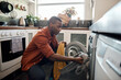 Young African man putting clothes in a washing machine at home