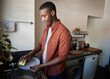 Young African man washing dishes in his kitchen at home