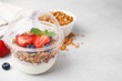 Tasty granola with berries and yogurt in plastic cup on light table, closeup. Space for text