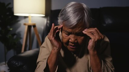 Wall Mural - senior woman having a headache pain while sitting on a sofa in living room at night