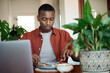Young African man using a laptop while eating breakfast