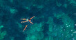 AERIAL, TOP DOWN: A woman and her kind dog swim together in the crystal waters