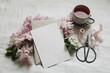 Breakfast still life. Spring stationery mockup. Pink blossoming Japanese cherry, apple tree branch. Blank greeting card, invitation. Cup of tea, black scissors. White linen table background. Flatlay
