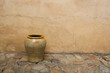 Rustic yellow clay vase on cobble stone floor, pavement against shabby ochre textured wall, house facade. Old French confit pot or vintage Spanish olive storage pot. Empty copy space, no people.