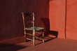 Old wooden one vintage chair in a room with red grunge walls and floor in sunlight, dark shadows. Shabby antique furniture. Empty copy space, no people. Retro interior still life, concept.