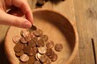 Donate and give concept. Woman putting coin into bowl at table, closeup