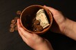 Donate and give concept. Woman holding bowl with coins and dollar banknotes at black wooden table, closeup