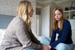 Mature Mother Sitting On Bed With Unhappy Teenage Daughter At Home Discussing Problem