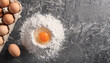 Wheat flour and chicken eggs on dark cooking background. Culinary and baking concept. Flat lay.