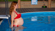 Pregnant red-haired woman in the pool in a red bikini. 