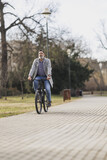 Fototapeta  - Man Riding a Bike Down a Sidewalk In the Park