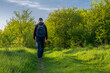 A man with a blue backpack walks along a path among green trees and young greenery. The concept of a walk to maintain health