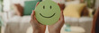 A person’s hands displaying a round, green smiley face, symbolizing positivity and happiness in a cozy home setting