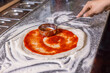 Closeup hand of chef baker making pizza at kitchen. The process of preparing pizza. Chef pours tomato sauce over the rolled dough. Chef hand is spreading pasteurized tomato paste onto a pizza base