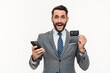 Happy Caucasian young businessman showing credit card and using cellphone isolated over white background. Online shopping e-banking e-commerce loan concept