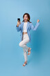 Portrait of a happy young asian woman celebrating with mobile phone isolated over blue background.