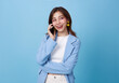 Happy Young Asian woman talking on the phone holds cellphone making answering call isolated on blue background