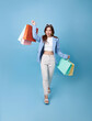 Happy pretty Asian woman carrying colorful shopping bags walking to supermarket isolated on blue background.