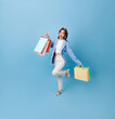 Happy pretty Asian woman carrying colorful shopping bags looking and pointing finger isolated on blue studio copy space background.