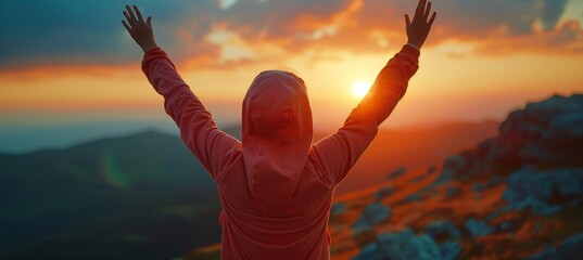 A young woman in a hoodie celebrates success at sunset on a mountain peak, captured in a panoramic banner with raised arms.