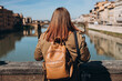 Rear view of redhead woman enjoys beautiful view on famous Old bridge in Florence. Female traveler visiting Italian landmarks. Concept of travel, tourism and vacation in city