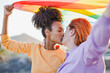 Happy lesbian multiracial women kissing each other while holding up rainbow flag outdoor - LGBT, love and gay pride parade concept