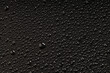 a large drop of water around which small drops on a black plastic surface