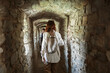 Curious tourist woman standing with backpack in stone passage of ancient castle. View from the back