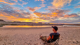 Fototapeta Góry - Man sitting on camping chair at Lone Rock beach campground with scenic sunrise view of Wahweap Bay at Lake Powell, Glen Canyon Recreation Area, Page, Utah, USA. Vanlife during sun down. Road trip